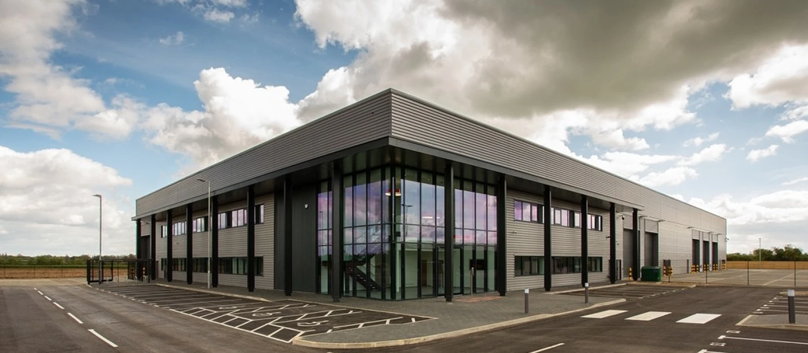 A large light grey bulding with a red roof, red panels around the doors and a large wall of wood panelling on one side